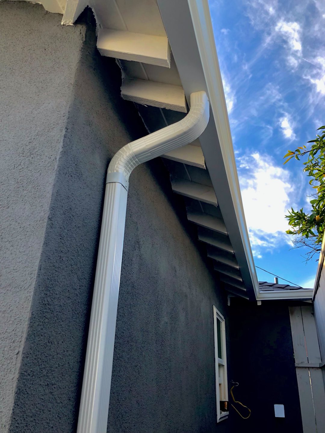 White corrugated downspout with a curved elbow on a gray stucco home in the Los Angeles area