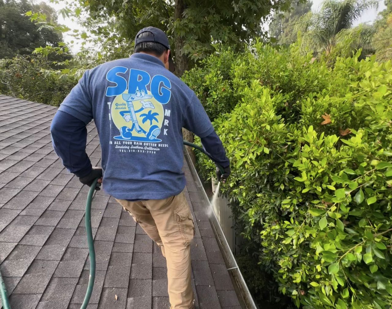 Gutter cleaning in the Los Angeles area: flushing a cleaned gutter with a hose from a shingle roof