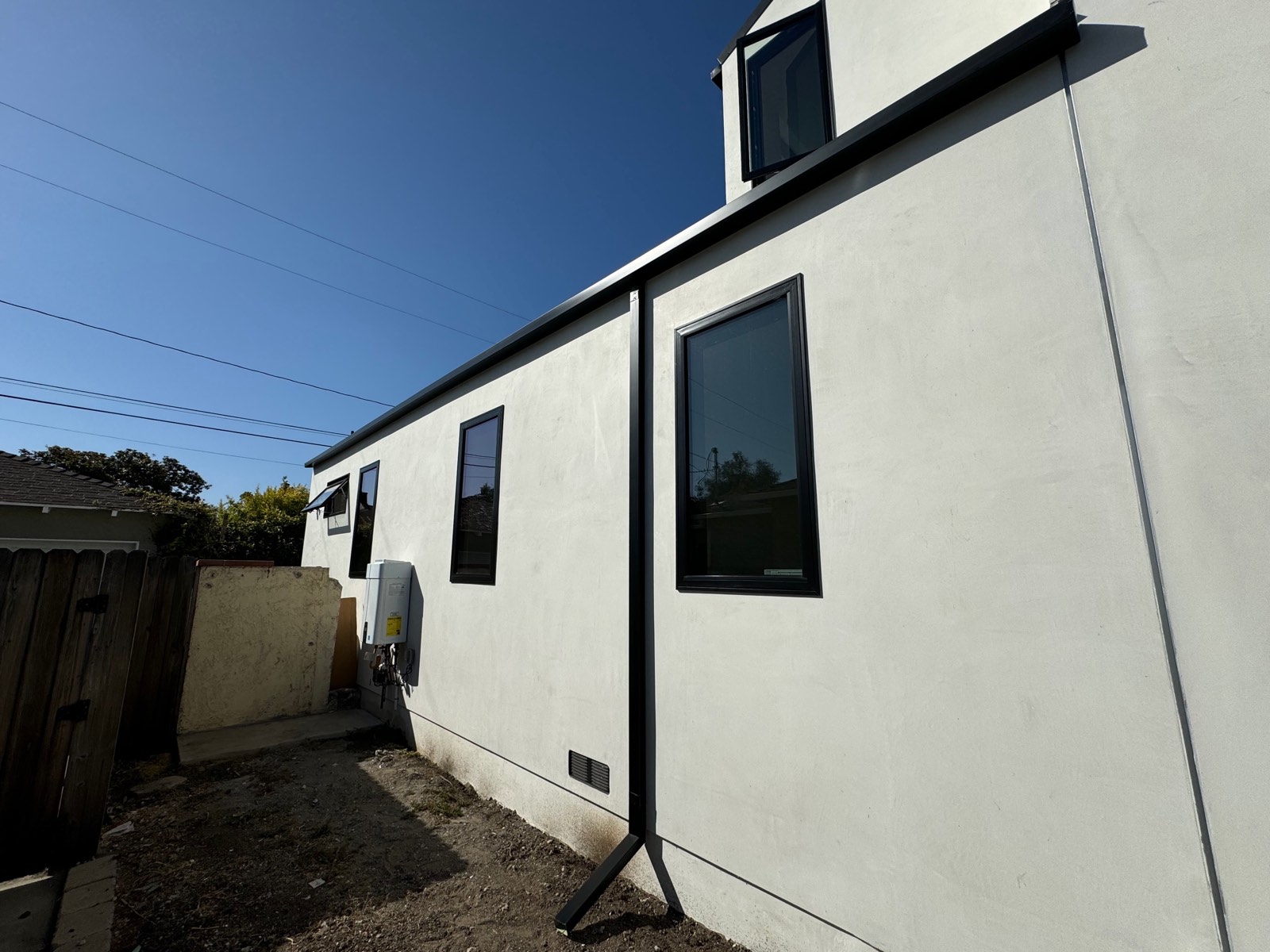 New black gutter and square downspout along the roofline of a white stucco home in the Los Angeles area